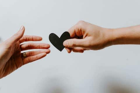 A person giving a paper heart to someone else.